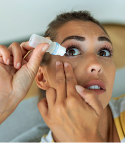 A woman applying medicated drops to their eye.